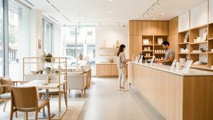 Intérieur lumineux d’un commerce moderne avec mobilier soigné, présentoirs élégants, comptoir et deux clients en train de regarder les produits.